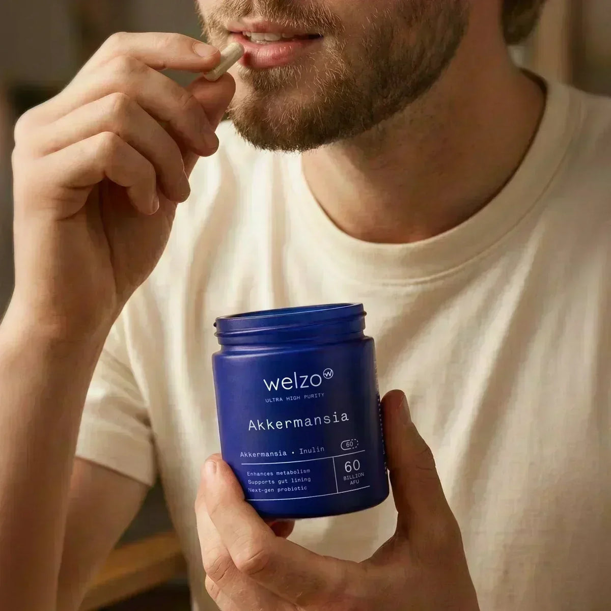 Person taking a Welzo Akkermansia muciniphila supplement capsule while holding the supplement bottle